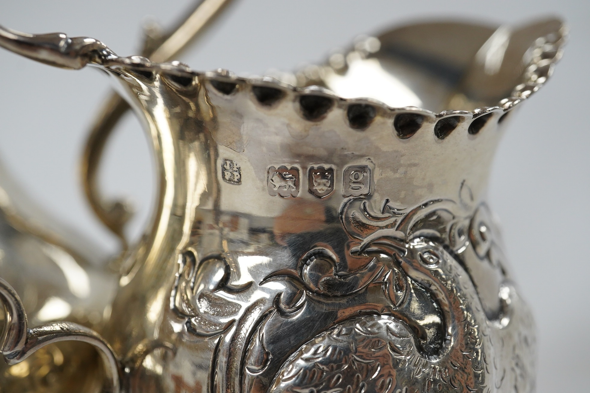 A Victorian engraved silver baluster cream jug, Henry Holland, London, 1862, 15cm, together with an Edwardian embossed silver cream jug, London, 1902, 10.5oz. Condition - poor